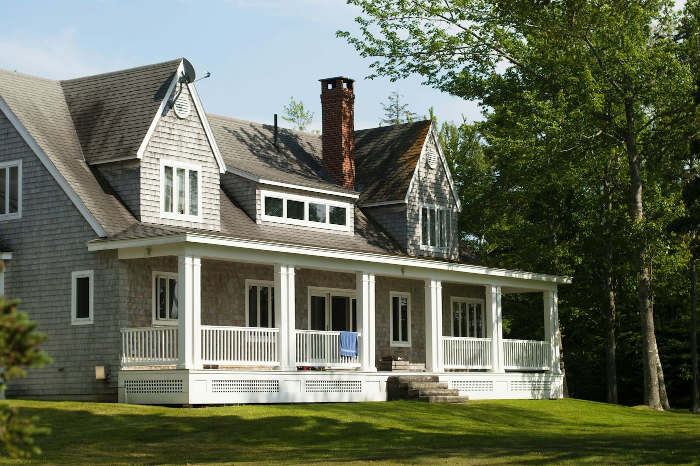Gray home with a wraparound porch framed by trees.